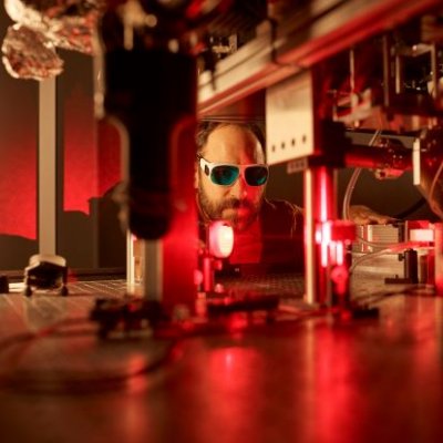 Male researcher under red light in a quantum physics lab.